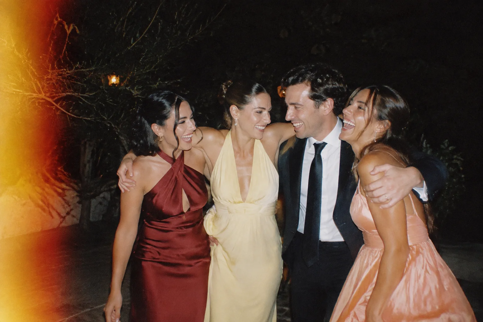 Friends in their wedding best, arm in arm under the night sky.