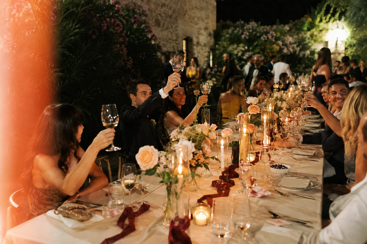 Guests raising a toast at a candlelit garden dinner.