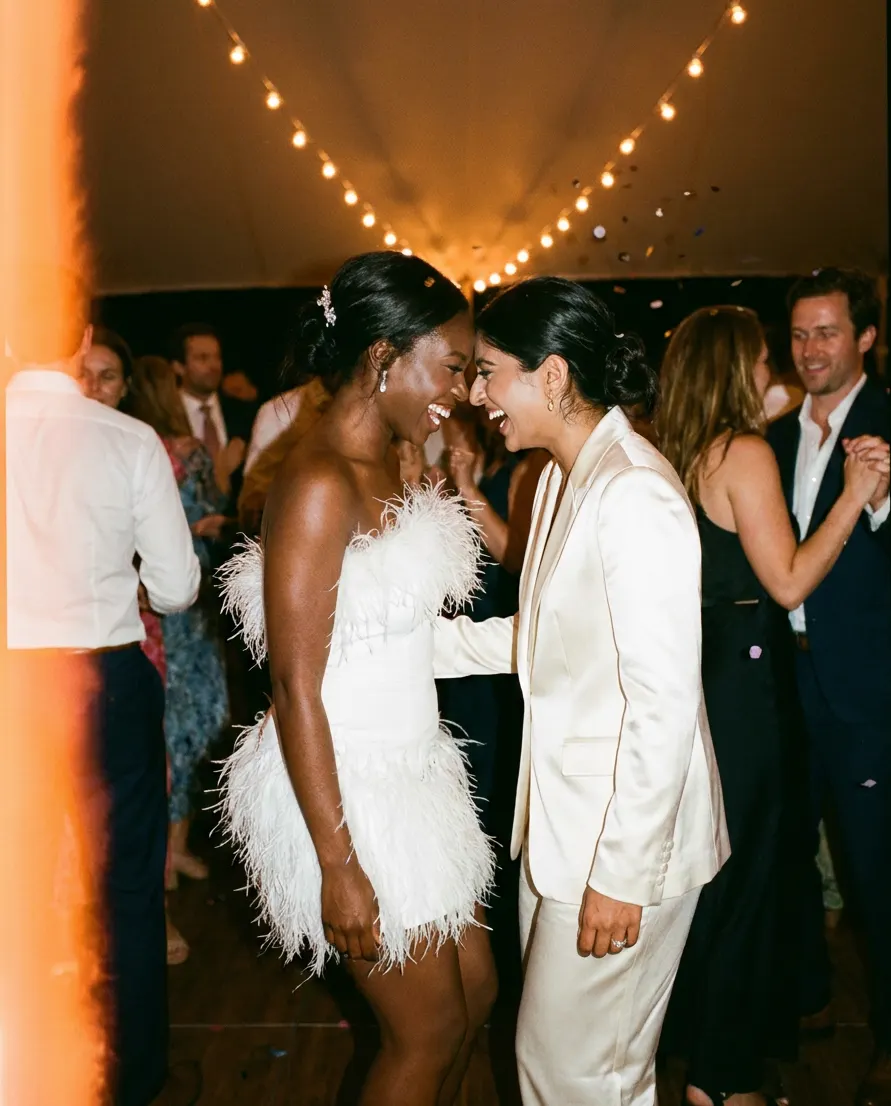 Two brides laughing together on a crowded dance floor.