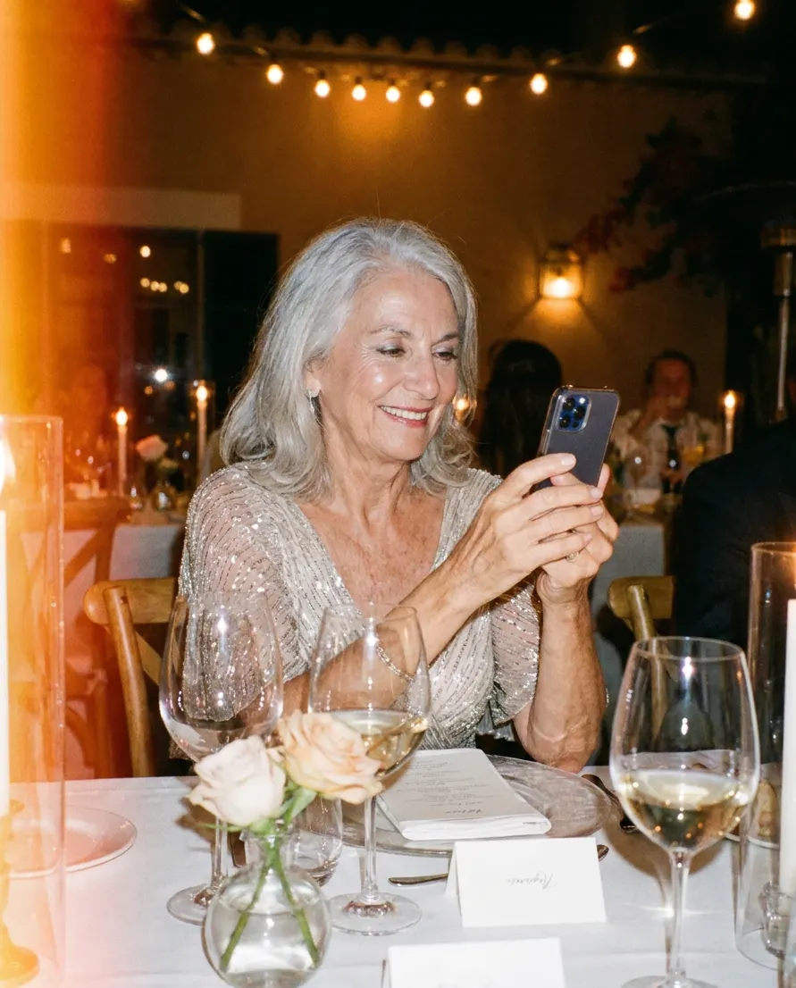 A grandmother taking a photo on her phone at the reception table.